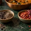 Black peppercorns and cracked pepper beside dried red chillies and chilli flakes
