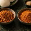 Two bowls showing coarse and fine podi beside idli