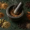 Whole and freshly ground Indian spices around a stone mortar