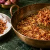 Golden fried onions being lifted from a kadai for biryani