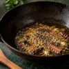 Cumin, mustard seeds and whole spices sizzling in oil in a black kadai