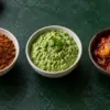 Three bowls containing dry podi, fresh green chutney and Indian pickle
