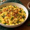 Bowl of fluffy poha topped with podi, beside lemon and a small bowl of seasoning