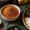 Bowl of podi beside rock salt and a plate of rice and vegetables