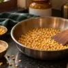 Golden roasted dal in a steel pan with bowls of raw chana and urad dal
