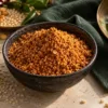 Bowl of coarse podi beside sesame seeds, roasted lentils and idlis