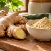 Fresh ginger rhizomes beside a bowl of dry ginger powder