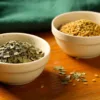 Separate bowls of dried fenugreek leaves and yellow-brown fenugreek seeds.