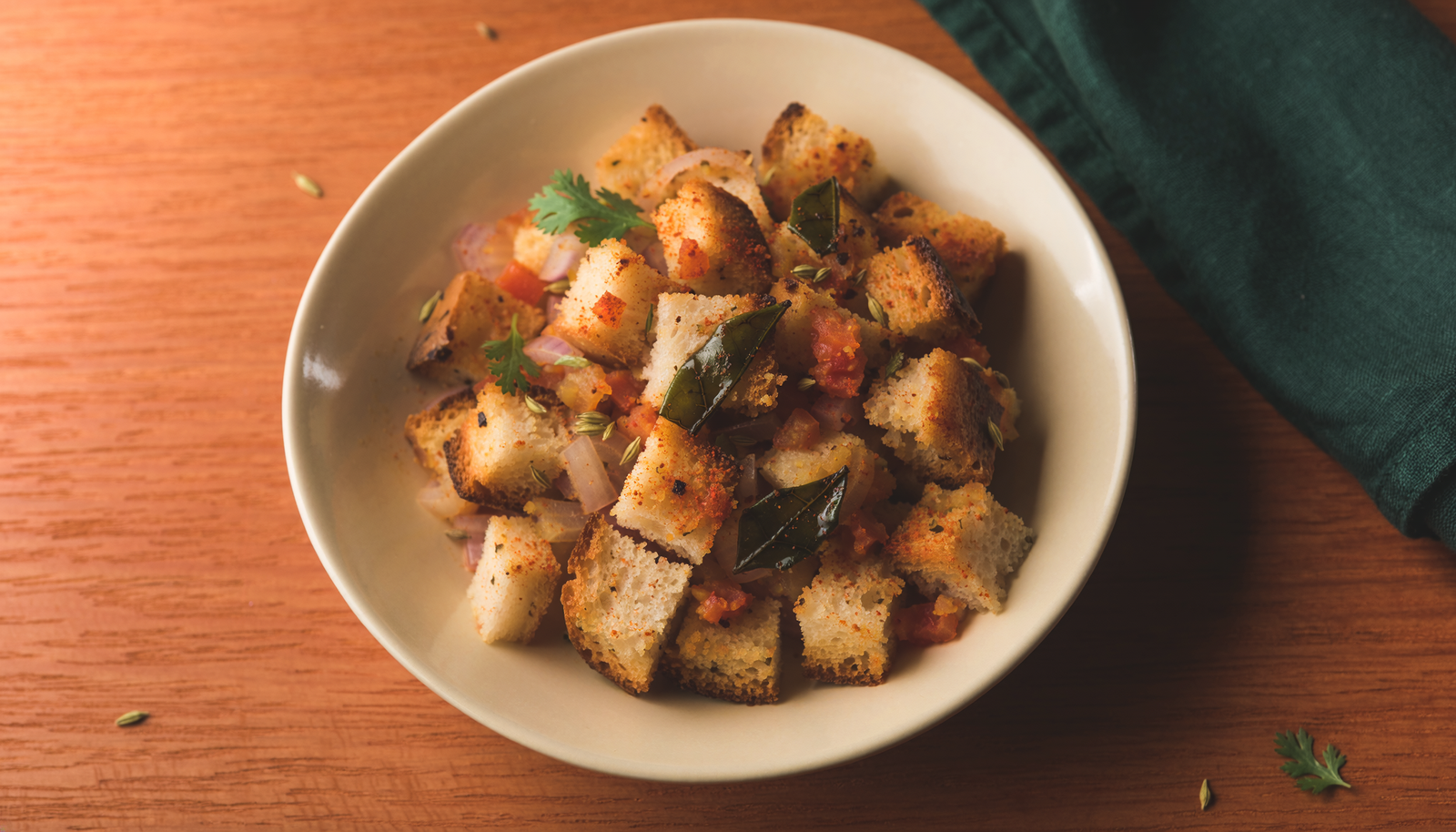 Close view of bread upma cubes with cooked tomato, onion and podi.