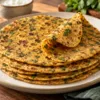 A stack of golden methi theplas with green fenugreek flecks