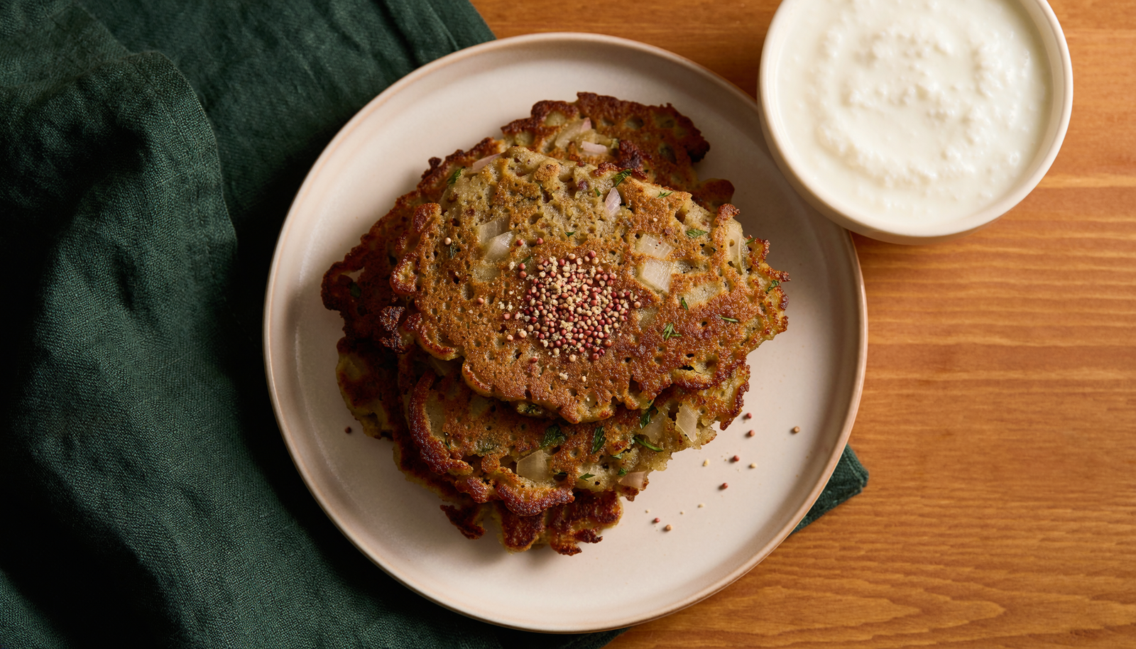 Overhead view of coarse millet and lentil adai with visible onion and a light podi sprinkle.